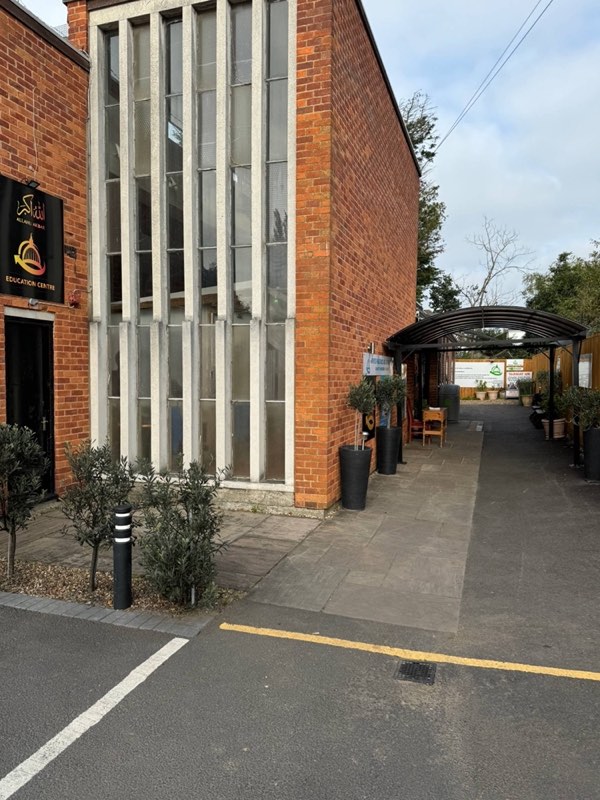 The entrance: an Allahu Akbar Education Centre sign on the brick wall, olive trees in planters, and a covered walkway leading along the building.