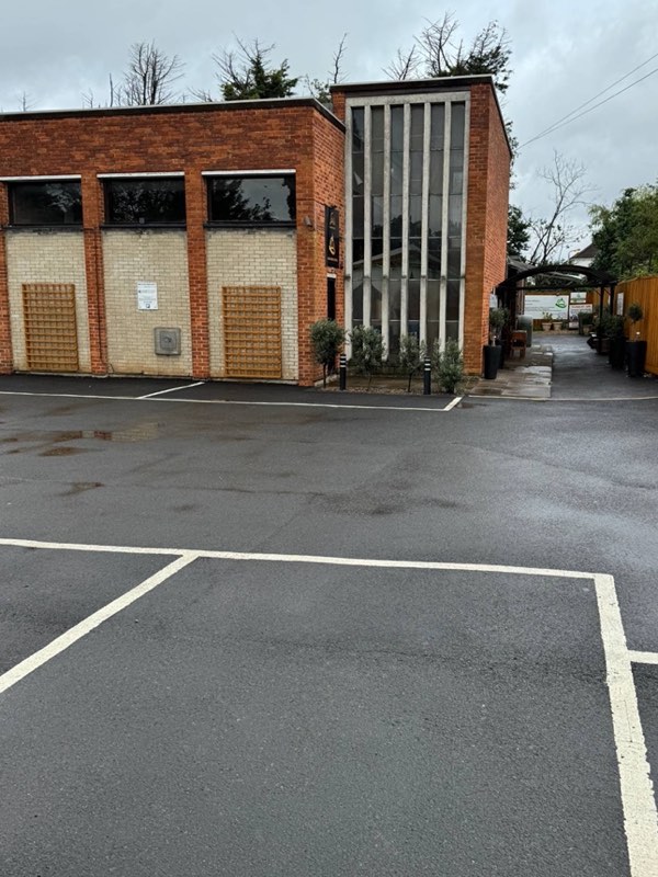 The masjid seen across its car park: a red-brick building with a tall, narrow window of concrete columns, and a covered walkway running down its side.